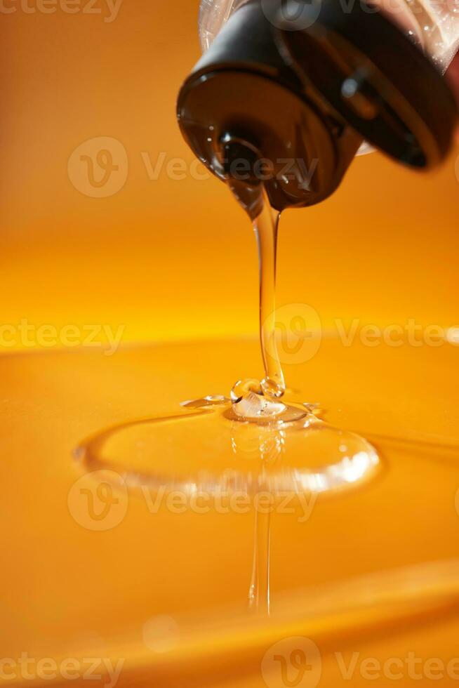 A drop of body gel or shampoo pouring from above on a yellow saturated background. photo