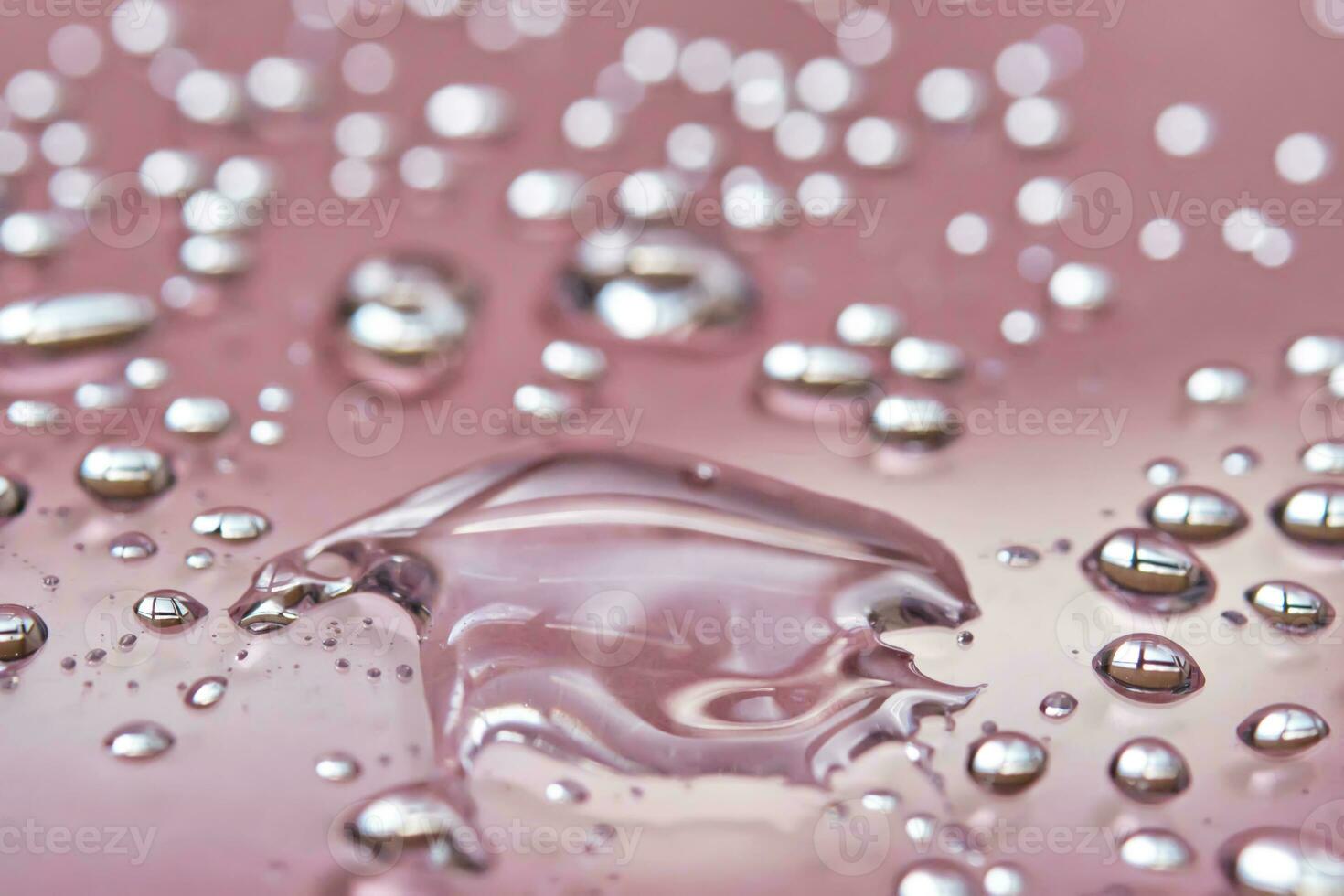 A large drop and splashes of micellar water on a pink background. photo