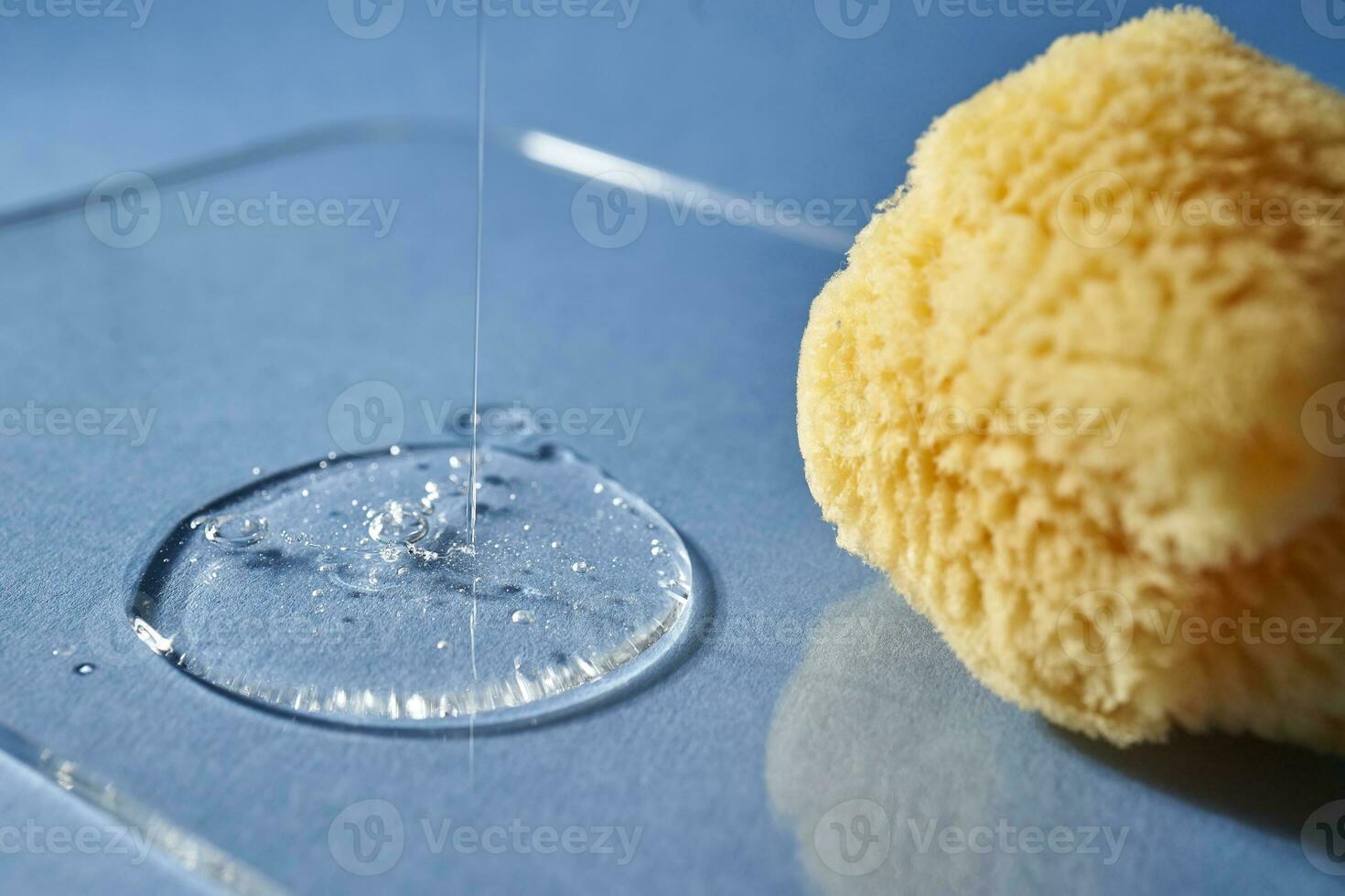 A natural sponge and a drop of gel or shampoo on a blue background. photo