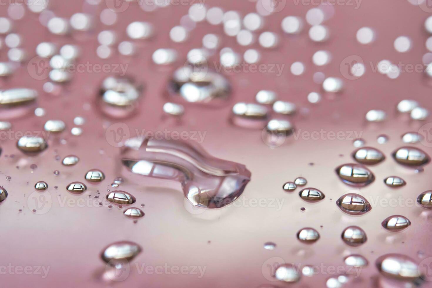 A large drop and splashes of micellar water on a pink background. photo
