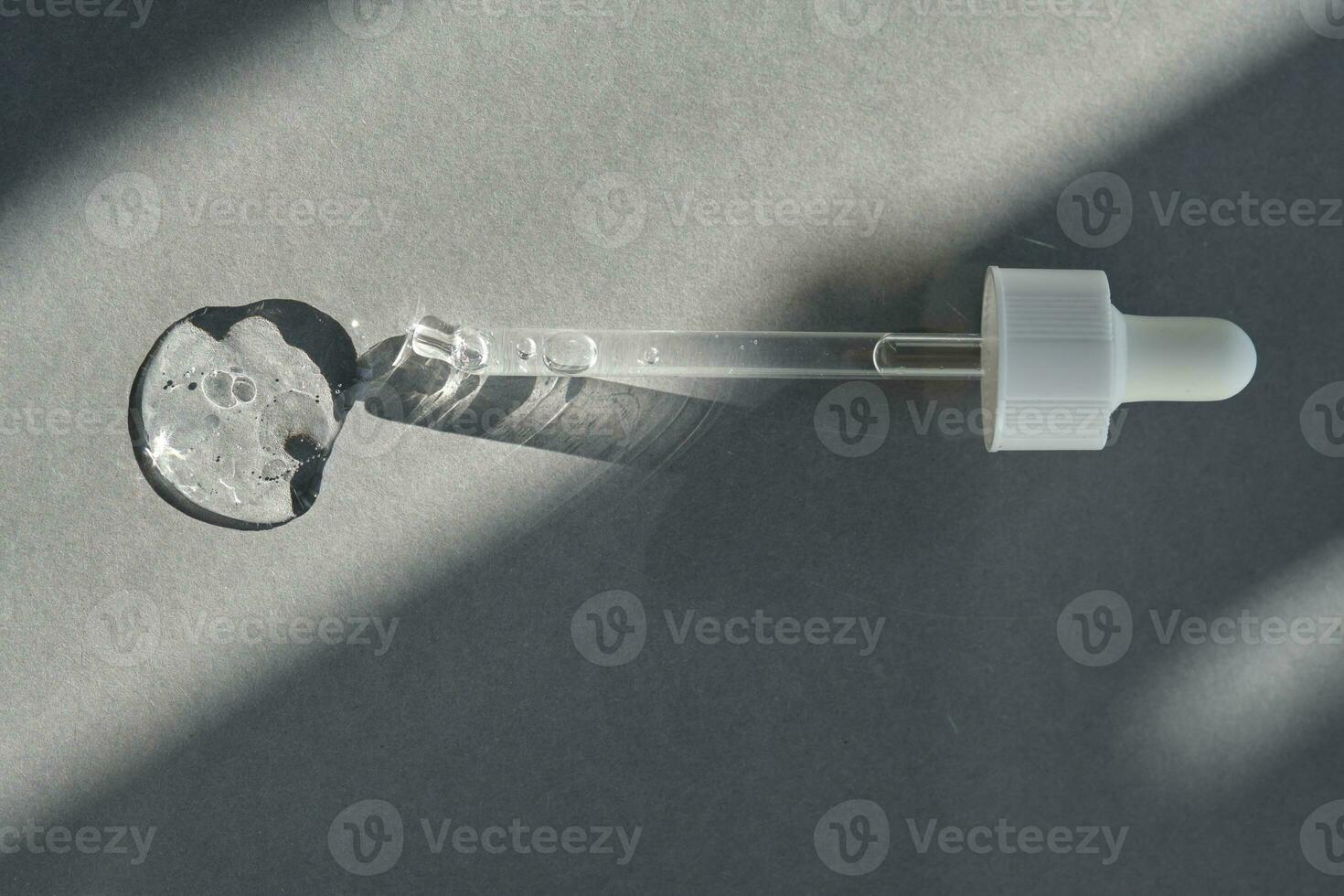 Pipette with spilled cosmetic oil or serum on a gray background. photo