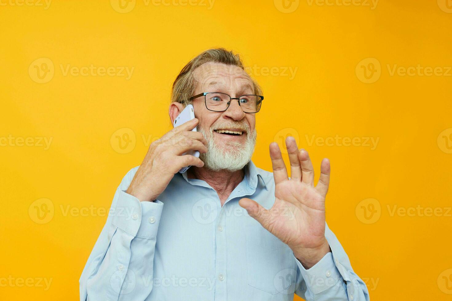Photo of retired old man gray beard with glasses talking on the phone yellow background