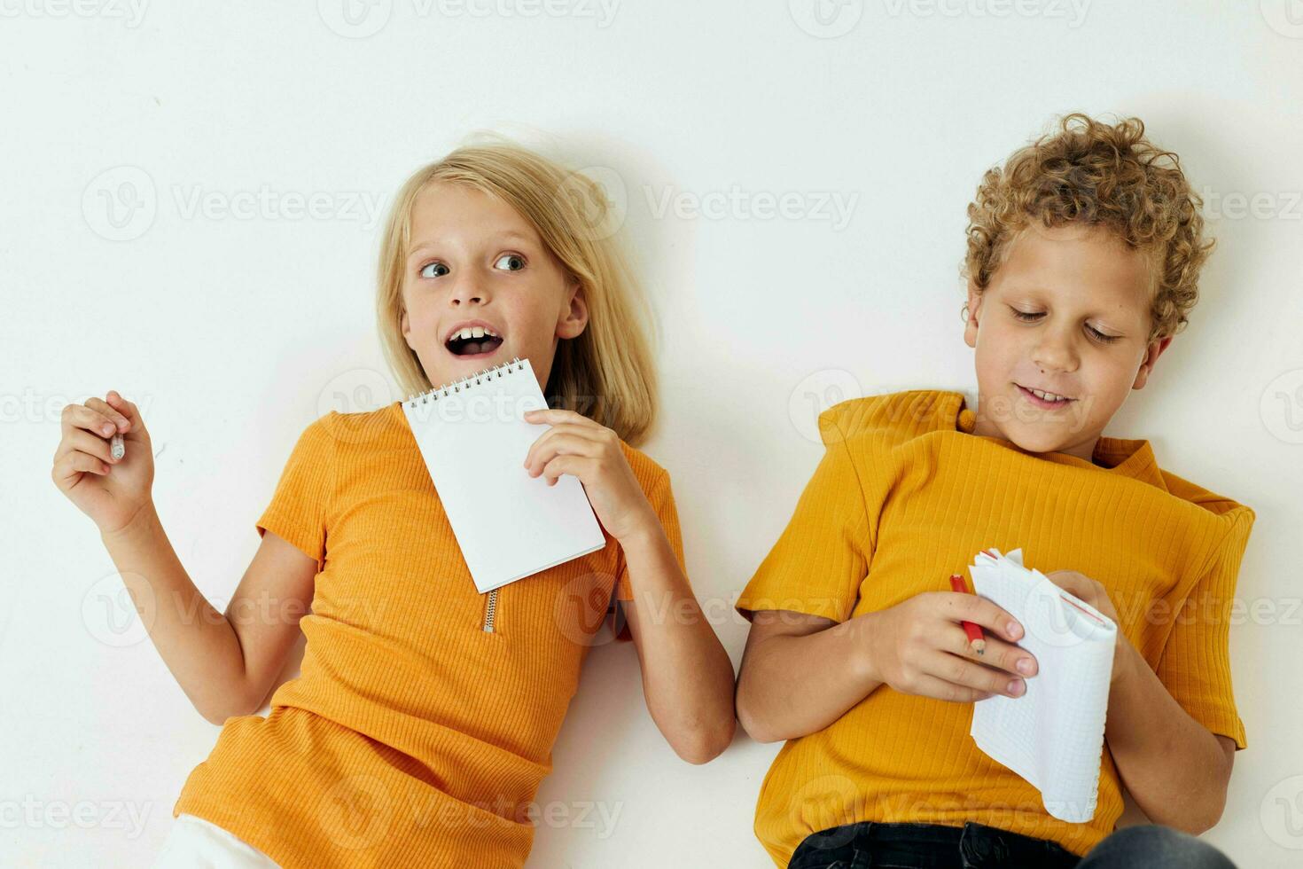 dos alegre niños dibujo en cuadernos acostado en el piso ligero antecedentes inalterado foto