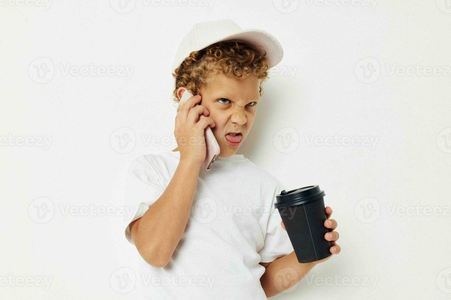 Cute little boy in a white t-shirt cap with a phone in a glass with a drink light background unaltered photo