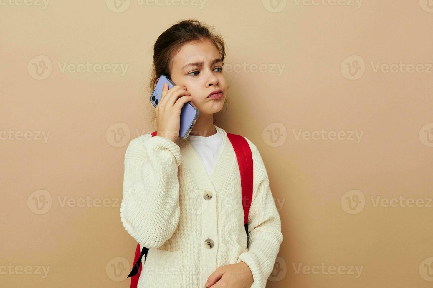 Portrait of happy smiling child girl talking on the phone with a backpack beige background photo