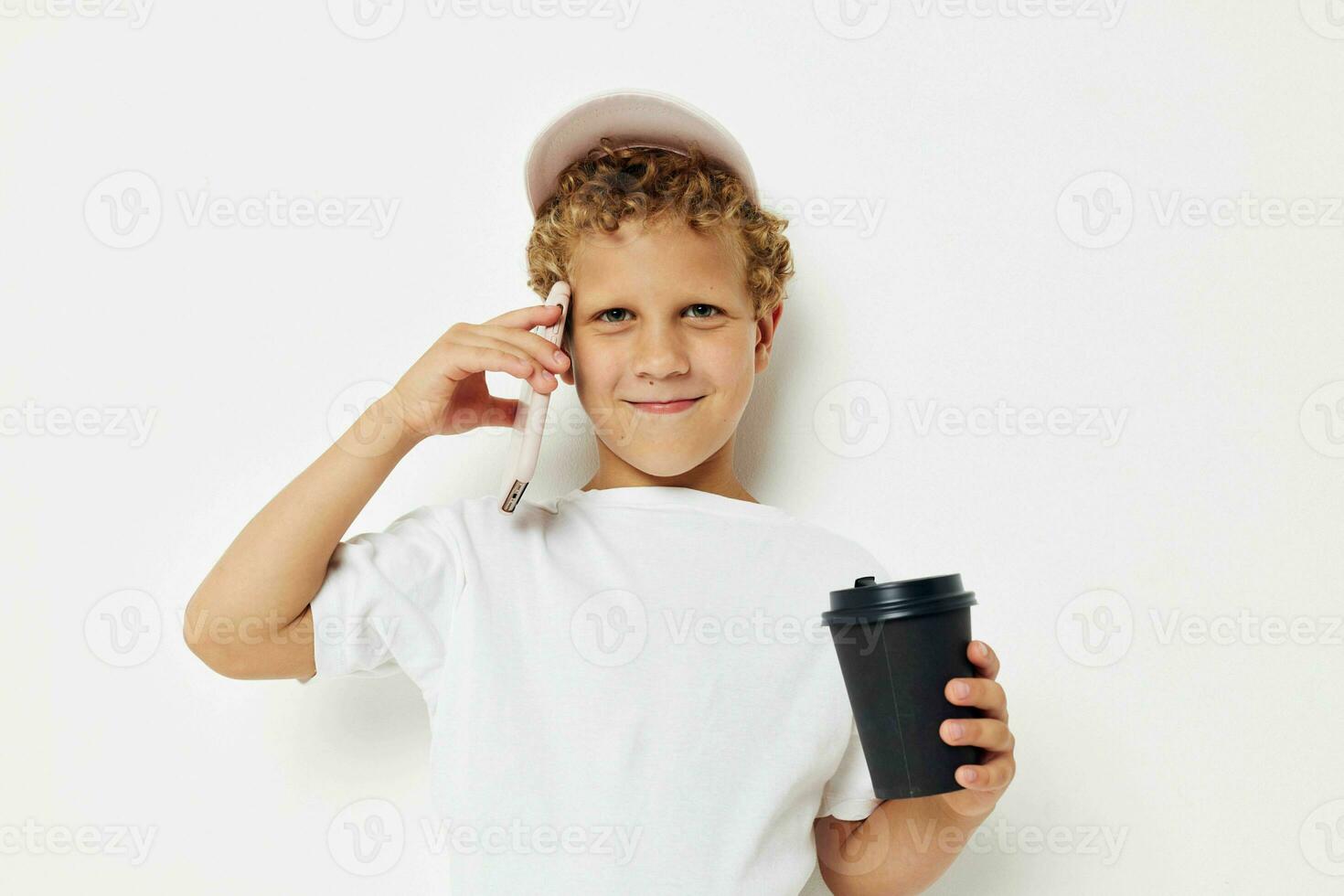 cute boy in a white t-shirt cap with a phone in a glass with a drink isolated background unaltered photo