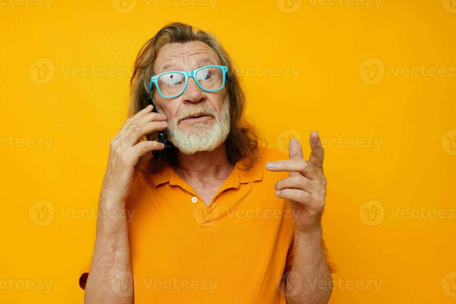 Portrait of happy senior man wearing blue glasses yellow shirt talking on the phone yellow background photo