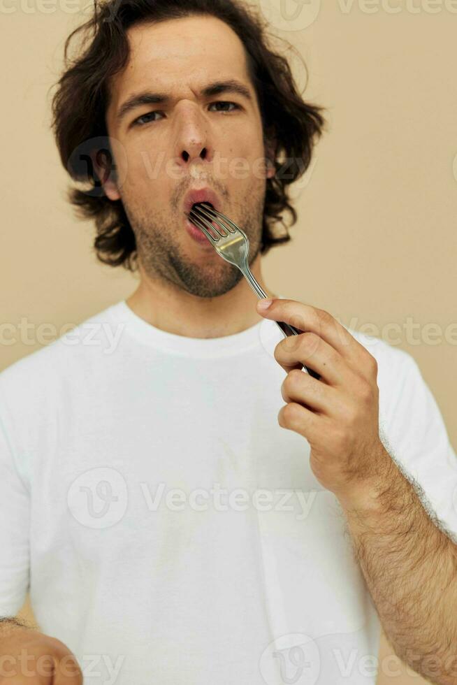 hermoso hombre en un blanco camiseta con cuchillo con tenedor beige antecedentes foto