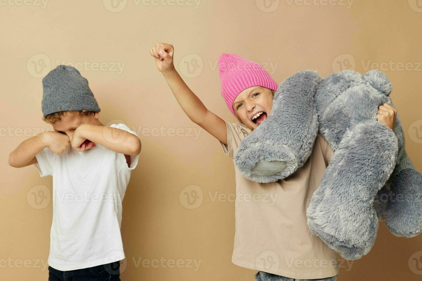 Photo of two children in multi-colored hats entertainment posing beige background