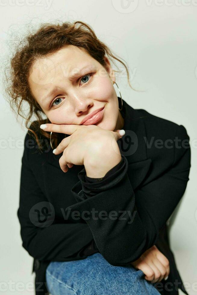 hermosa mujer sentado en un silla en un negro chaqueta Moda posando ligero antecedentes inalterado foto