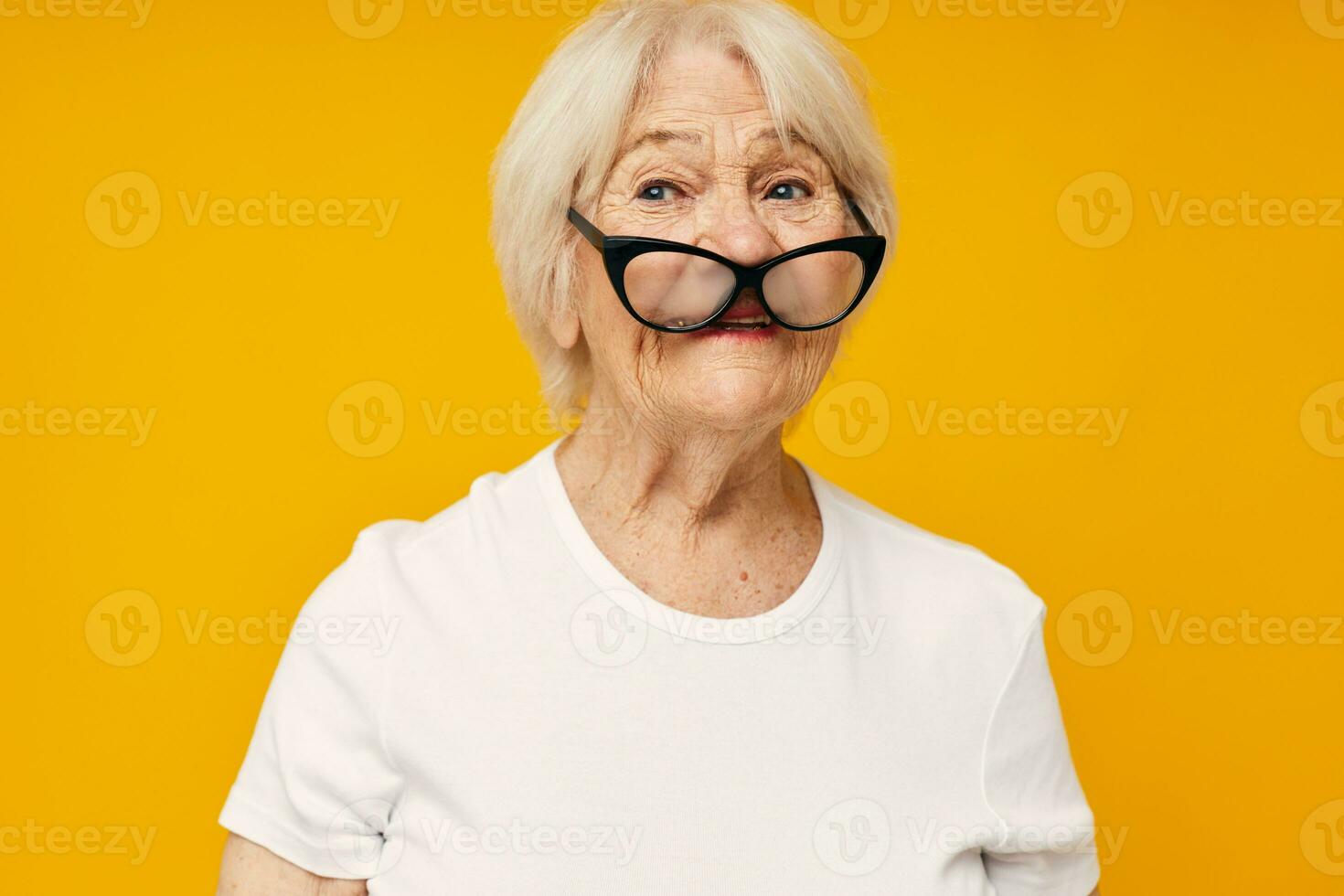 retrato de un antiguo simpático mujer en un blanco camiseta usa lentes aislado antecedentes foto