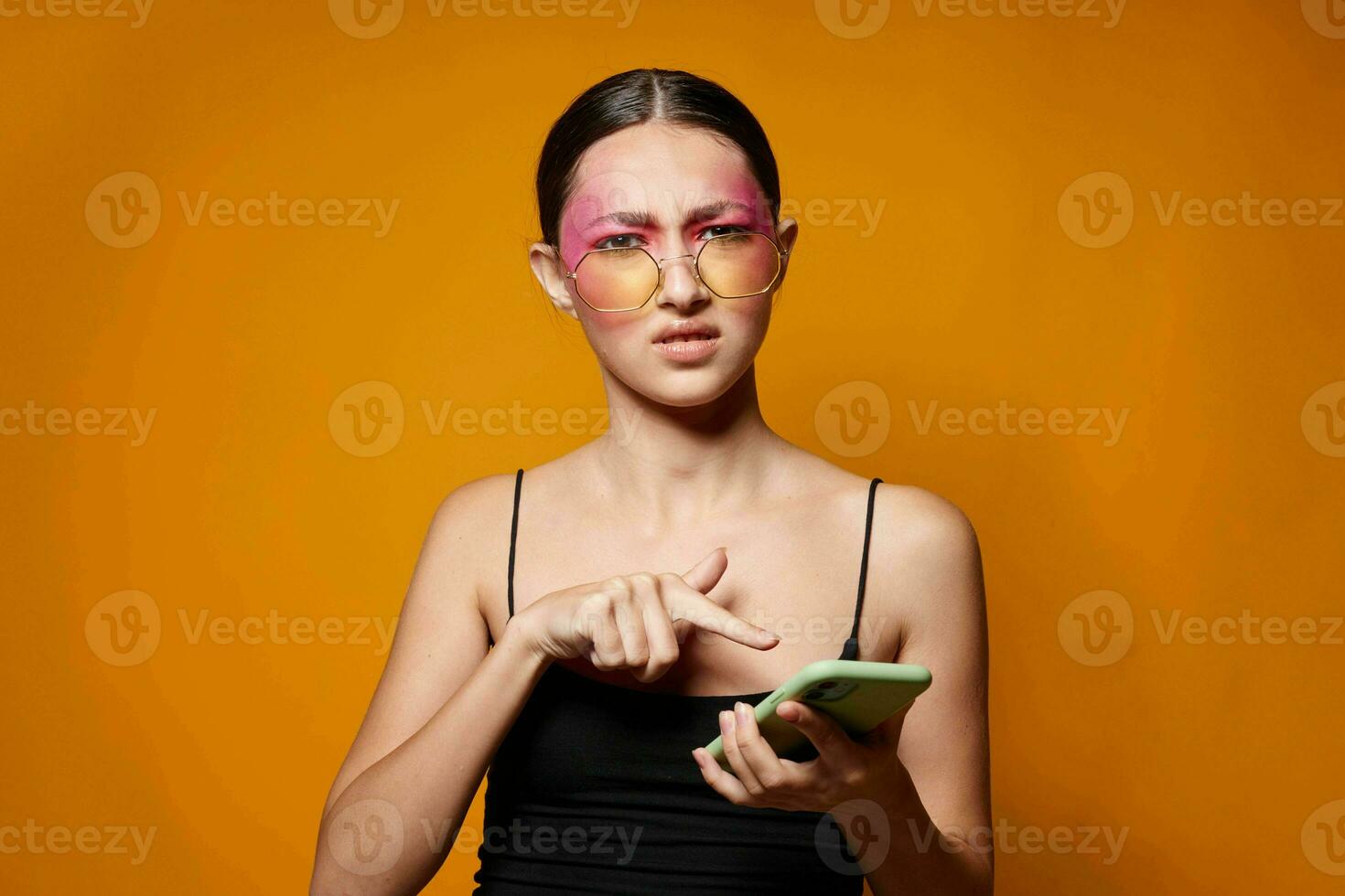 fashionable woman with phone pink face makeup posing attractive look glasses yellow background unaltered photo