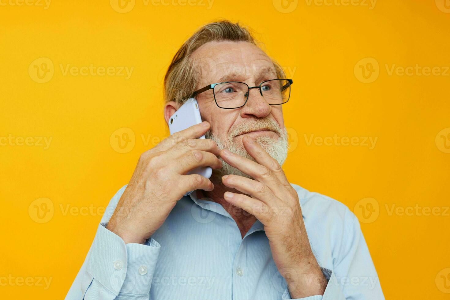 Photo of retired old man gray beard with glasses talking on the phone yellow background