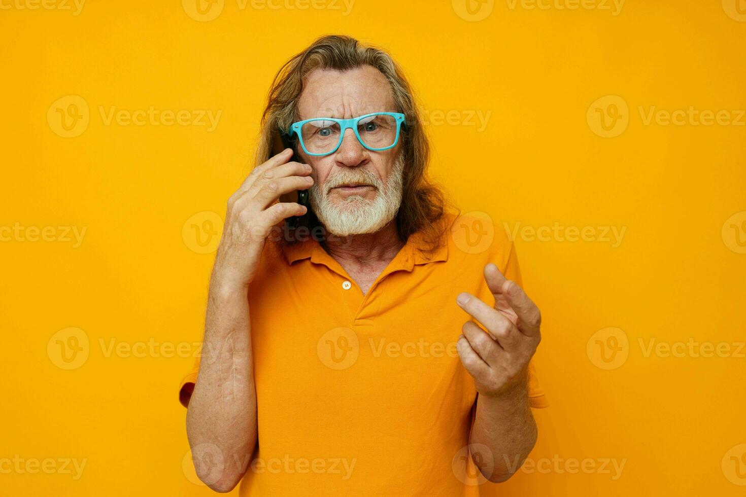Senior grey-haired man wearing blue glasses yellow shirt talking on the phone isolated background photo