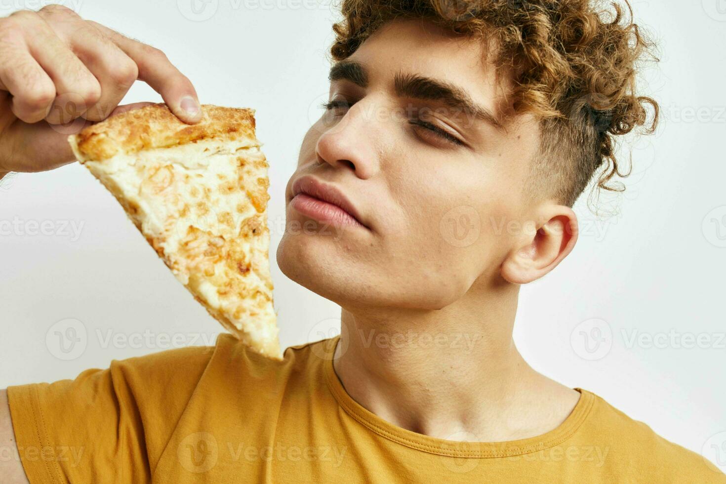 hermoso chico en un amarillo camiseta comiendo Pizza aislado antecedentes foto