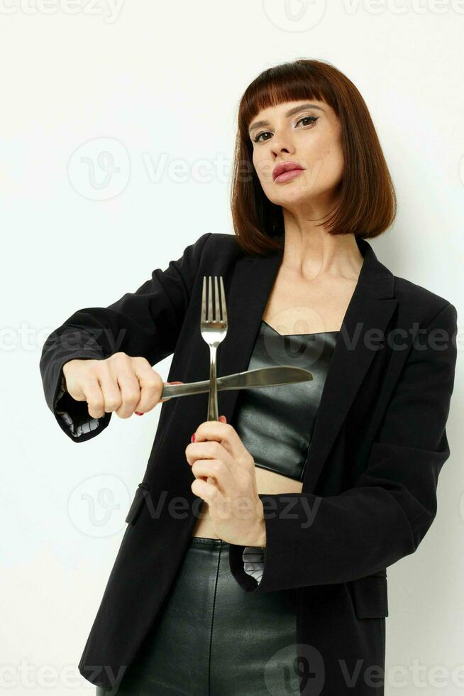 photo pretty woman in a black jacket a knife and a fork near the face light background
