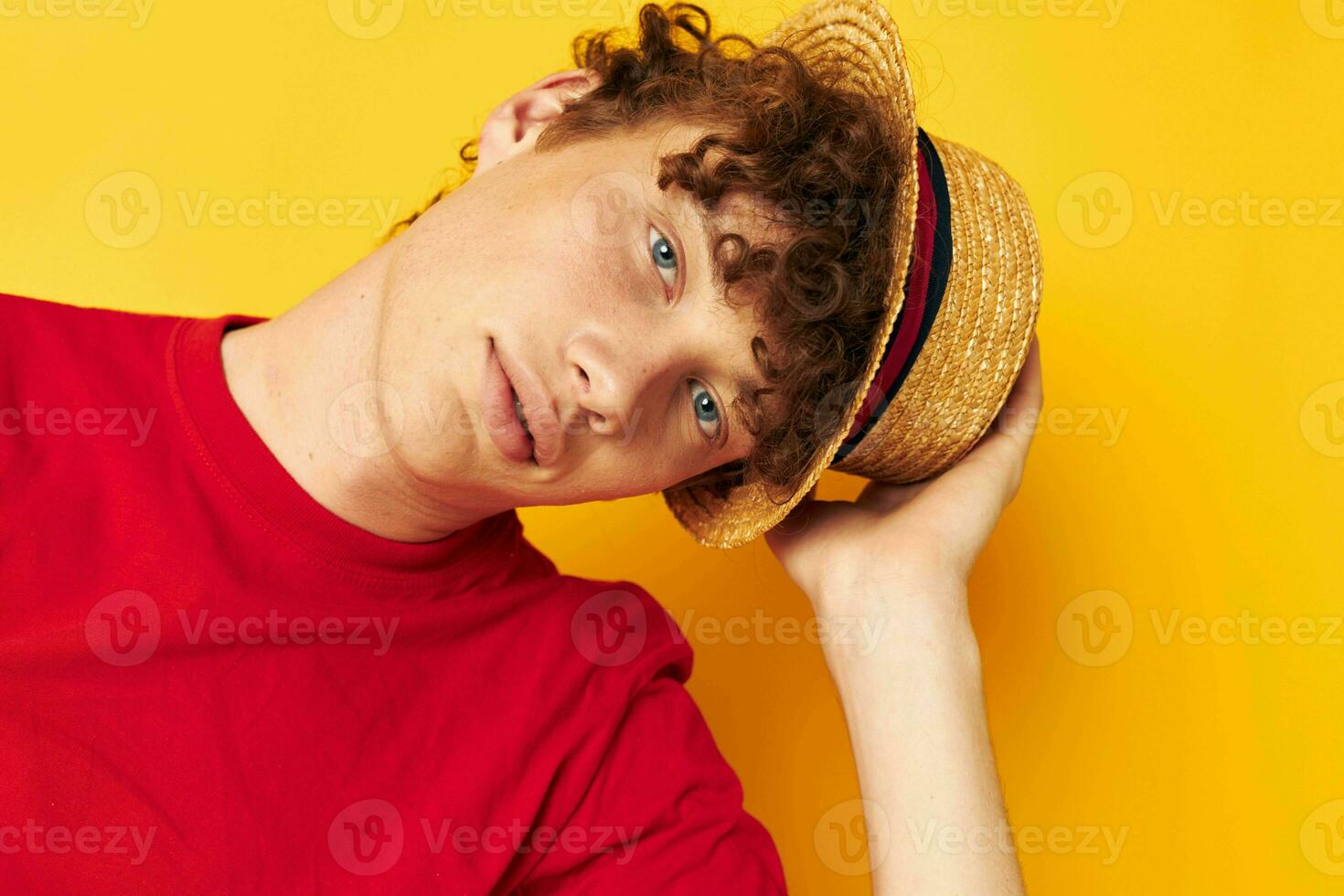 Young curly-haired man emotions red t-shirt hat studio yellow background unaltered photo