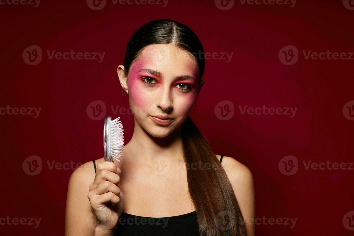 fashionable woman pink face makeup posing attractive look with a comb pink background unaltered photo
