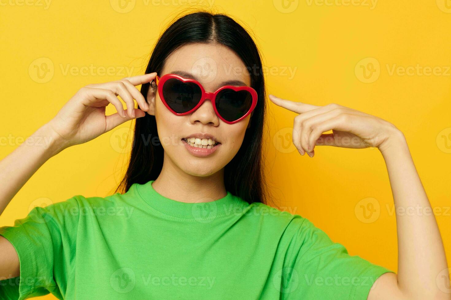 Charming young Asian woman in dark glasses in a green t-shirt posing modern yellow background unaltered photo