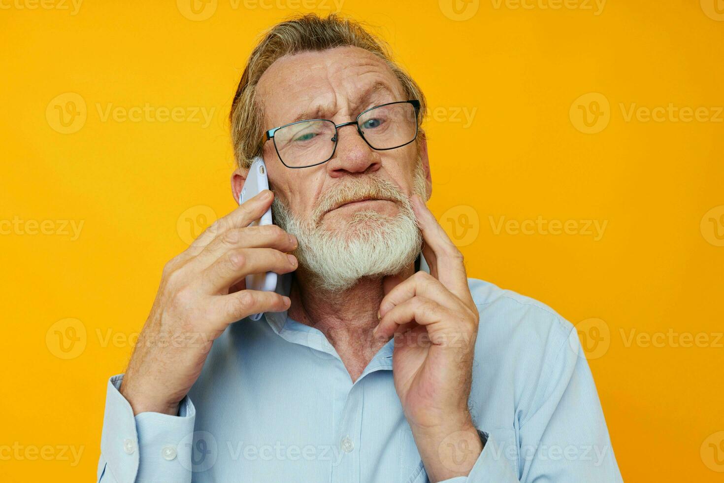 old man in a blue shirt and glasses talking on the phone yellow background photo