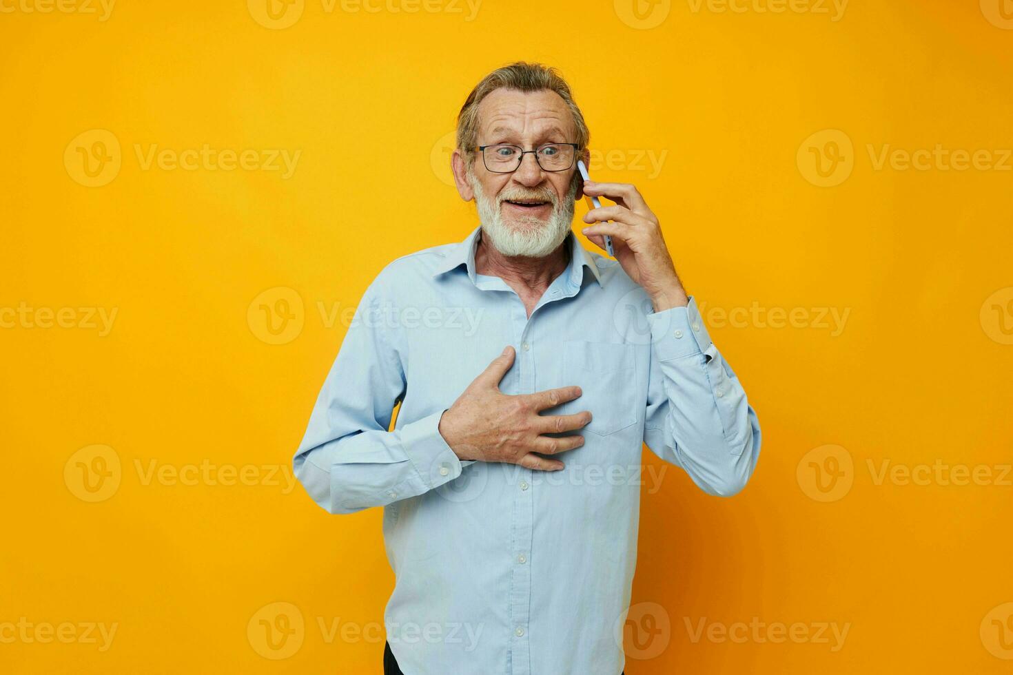 Portrait of happy senior man gray beard with glasses talking on the phone yellow background photo