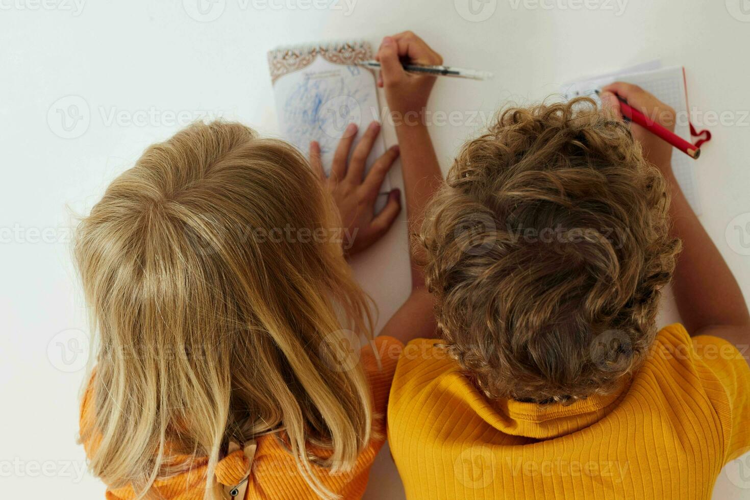 two joyful children drawing in notebooks lying on the floor light background unaltered photo