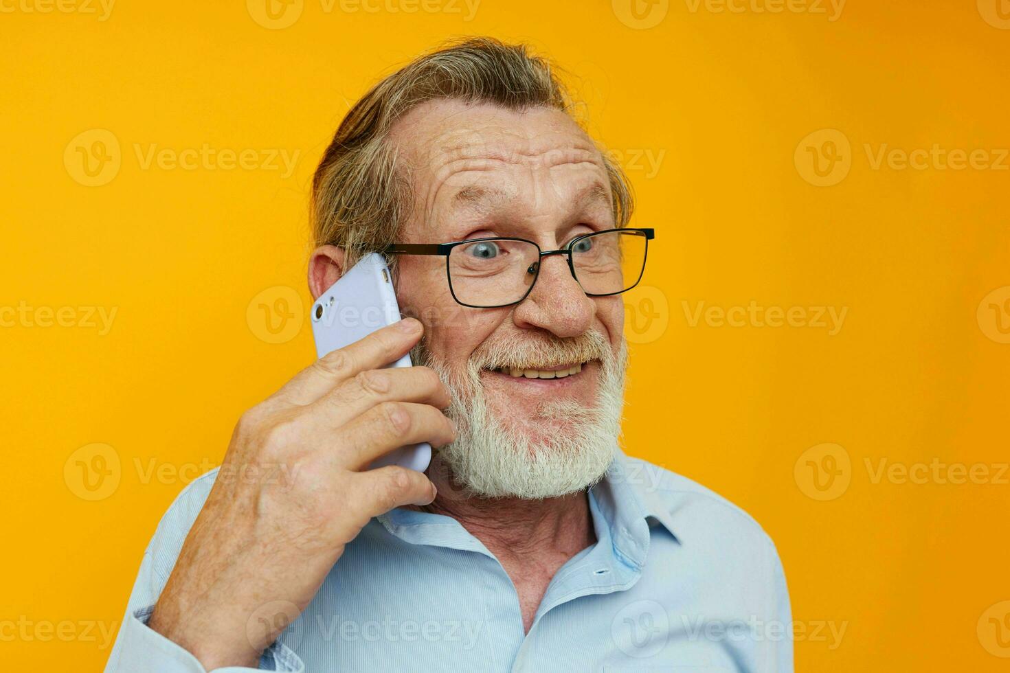 Portrait elderly man gray beard with glasses talking on the phone yellow background photo
