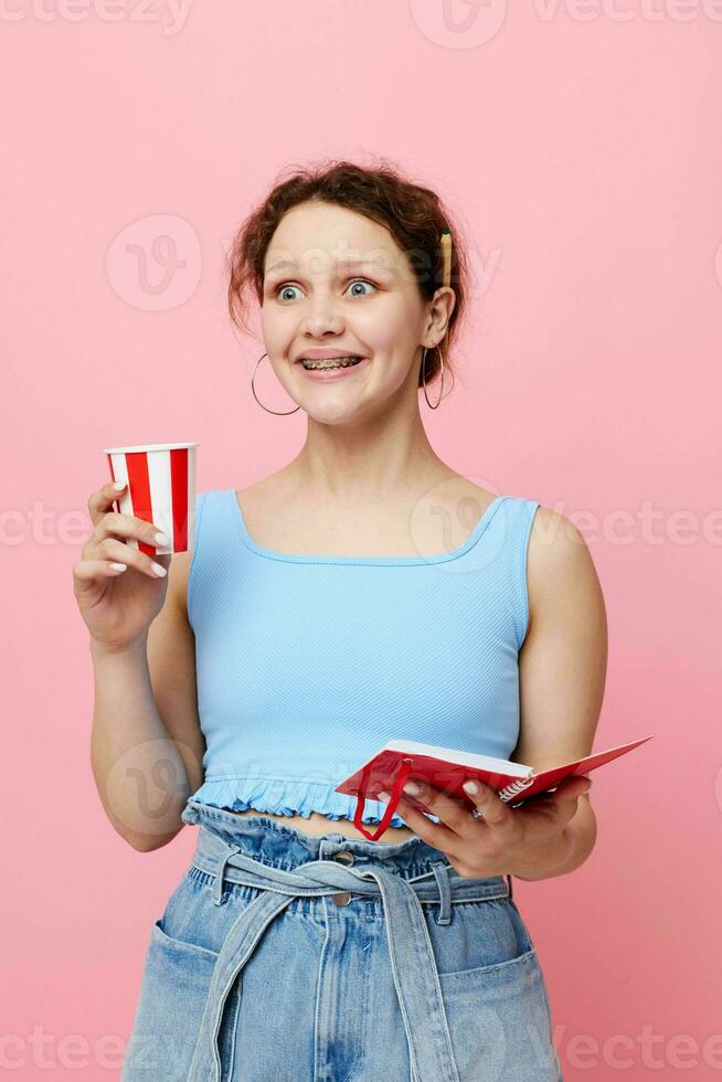 cheerful woman holding a notebook in her hands disposable glass drink pink background unaltered photo
