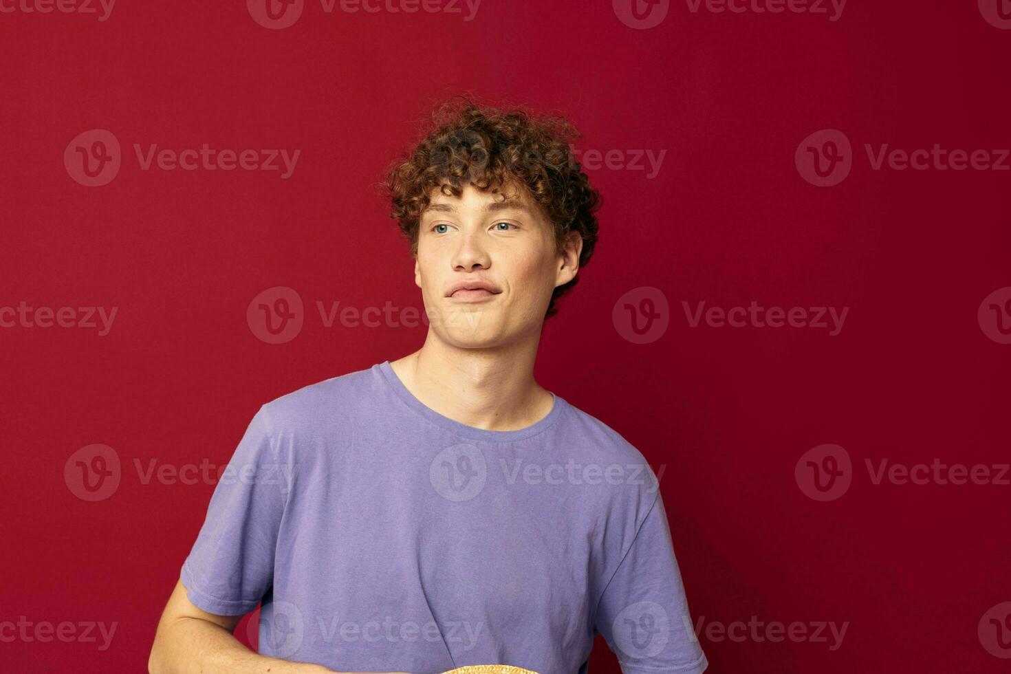 A young man in Hat purple t-shirts posing emotions red background unaltered photo