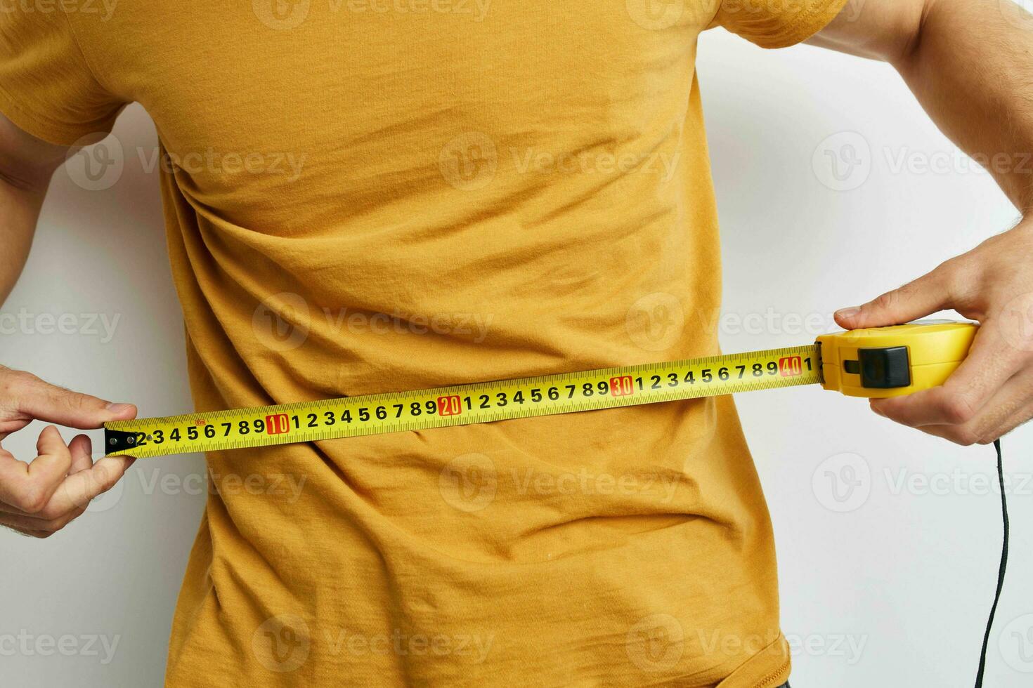 handsome guy measuring tape measure in yellow t-shirt light background photo