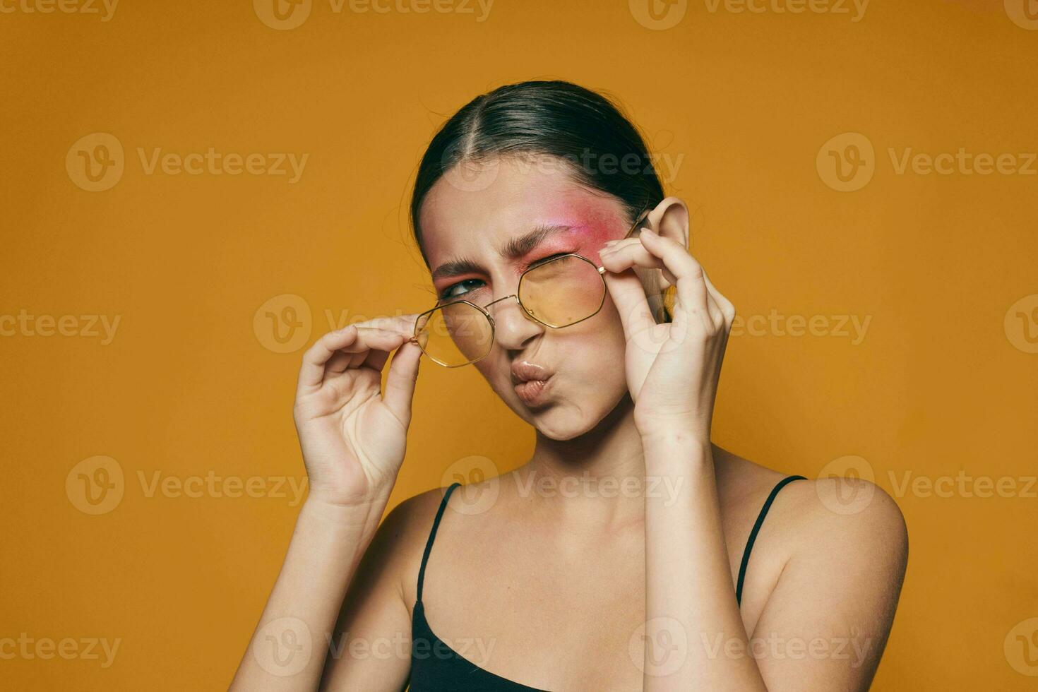 Portrait of beautiful young woman fashion glasses pink face makeup posing attractive look yellow background unaltered photo