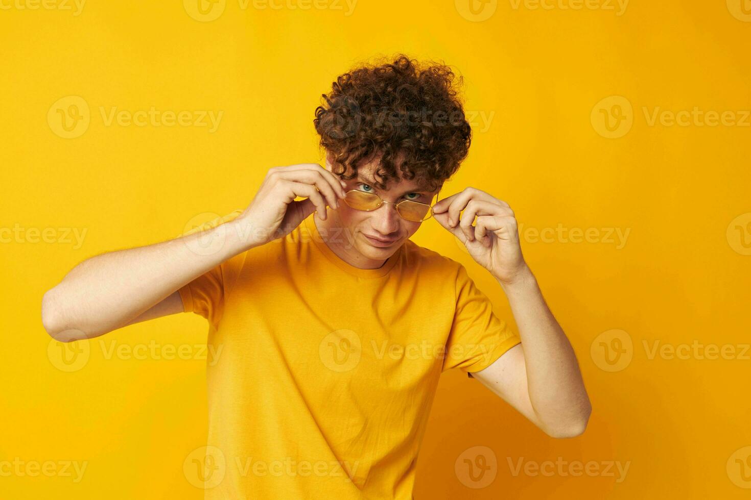Young curly-haired man yellow t-shirt glasses fashion hand gestures monochrome shot photo