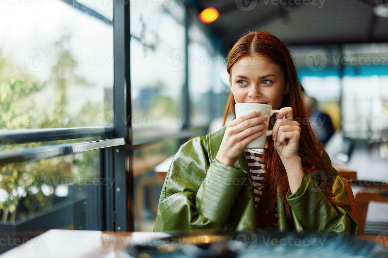 Stylish Influencer woman drinking a drink from a mug in a cafe and smiling looking out the window, content blogger photo