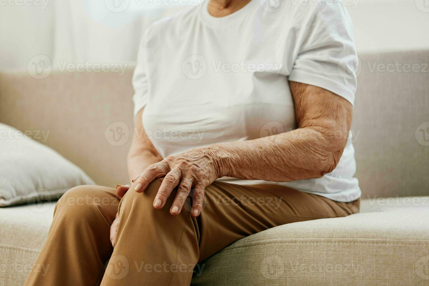 mayor mujer grave dolor en su pierna sentado en el sofá, salud problemas en antiguo edad, pobre calidad de vida. abuela con gris pelo sostiene en a su dolorido rodilla, problemas con articulaciones y ligamentos foto