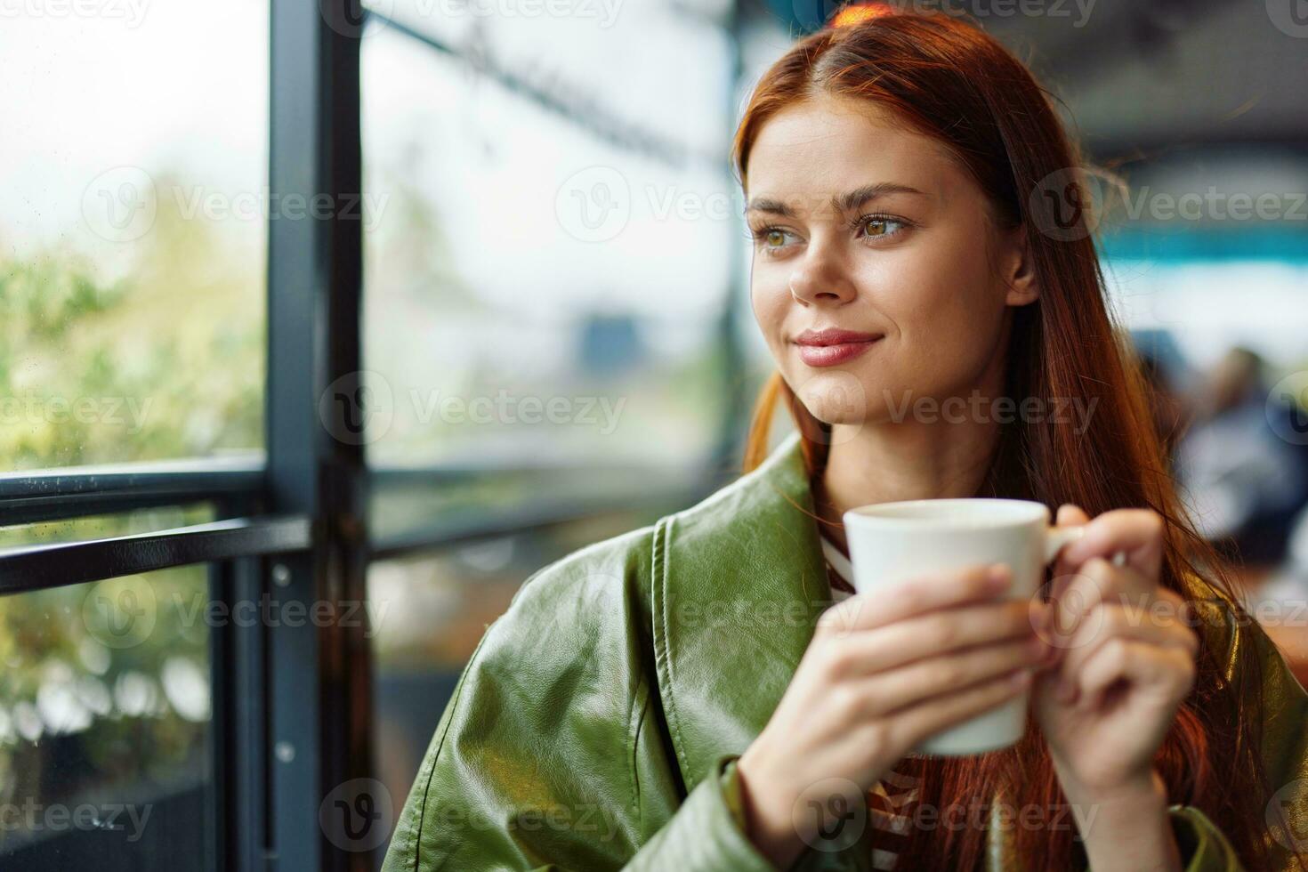 Portrait of a woman influencer drinking a drink from a mug in a cafe and smiling looking out the window, content blogger close-up photo