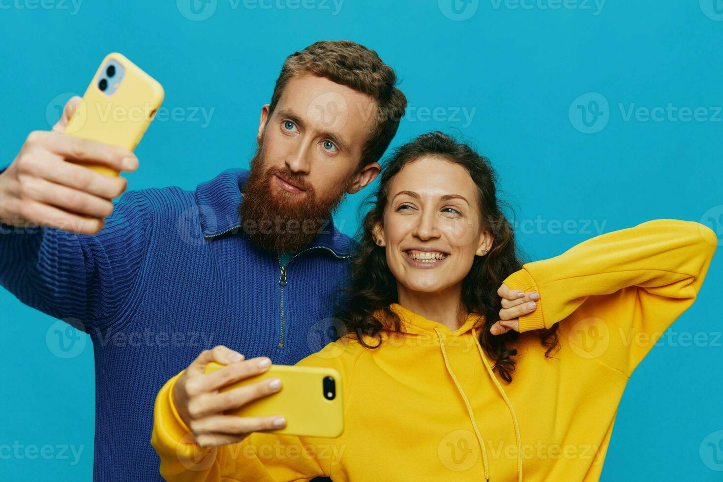 Woman and man funny couple with phones in hand taking selfies crooked smile fun, on blue background. The concept of real family relationships, talking on the phone, work online. photo