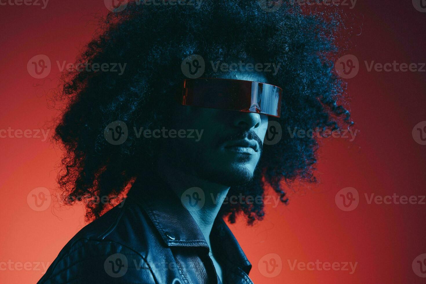 Portrait of fashion man with curly hair on red background with stylish glasses, multicultural, colored light, black leather jacket trend, modern concept. photo