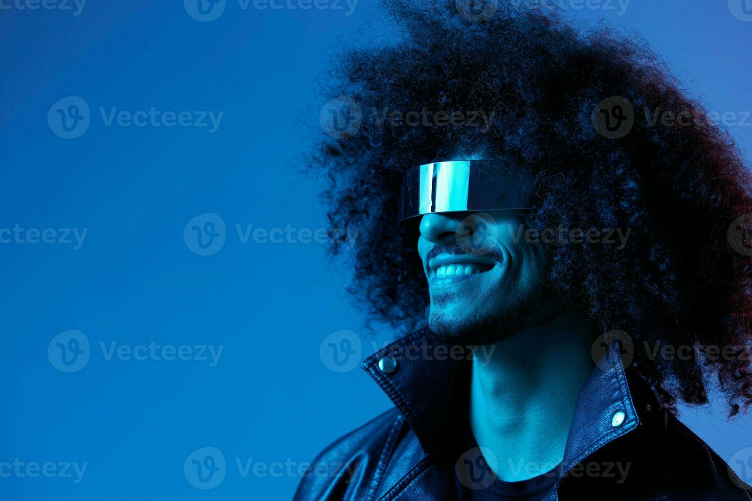 Portrait of fashion man with curly hair with stylish glasses on blue background multinational, colored light, black leather jacket trend, modern concept. photo