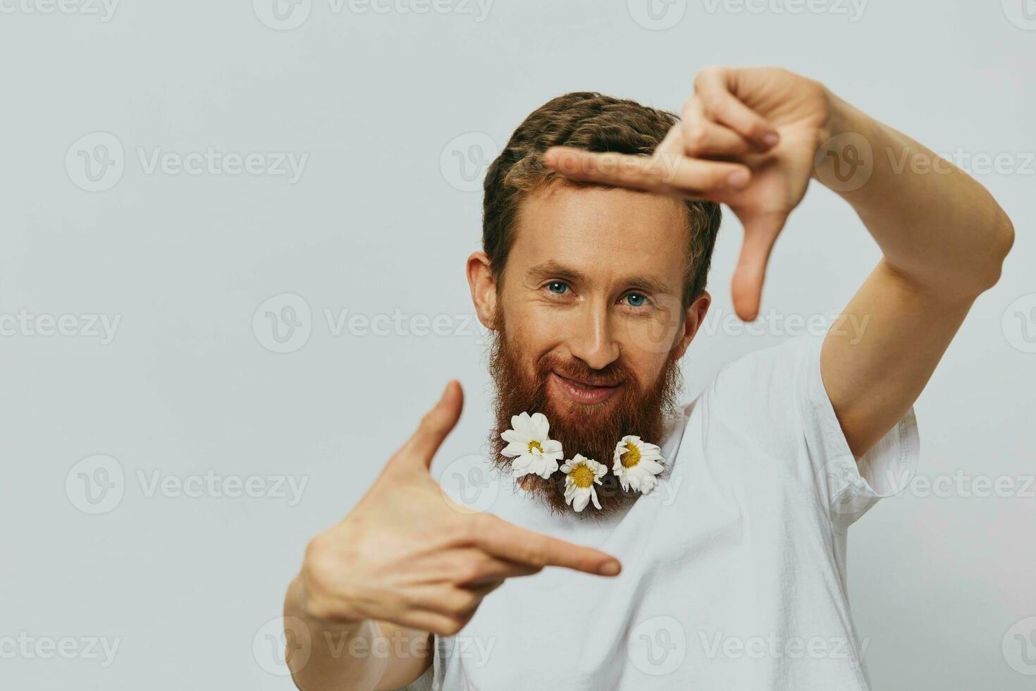 Portrait of a funny man in a white T-shirt with flowers daisies in his beard on a white isolated background, copy place. Holiday concept and congratulations. photo