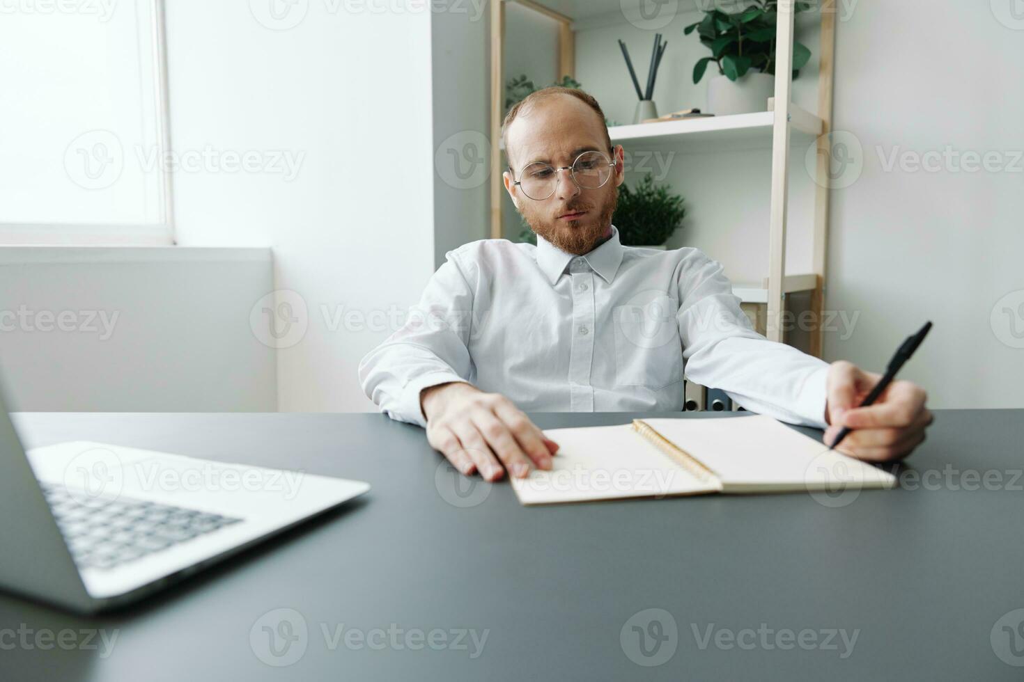 A man in a wheelchair, a businessman in the office works at a laptop, writing down a plan in a notebook, thoughtfulness, integration into society, the concept of working a person with disabilities photo