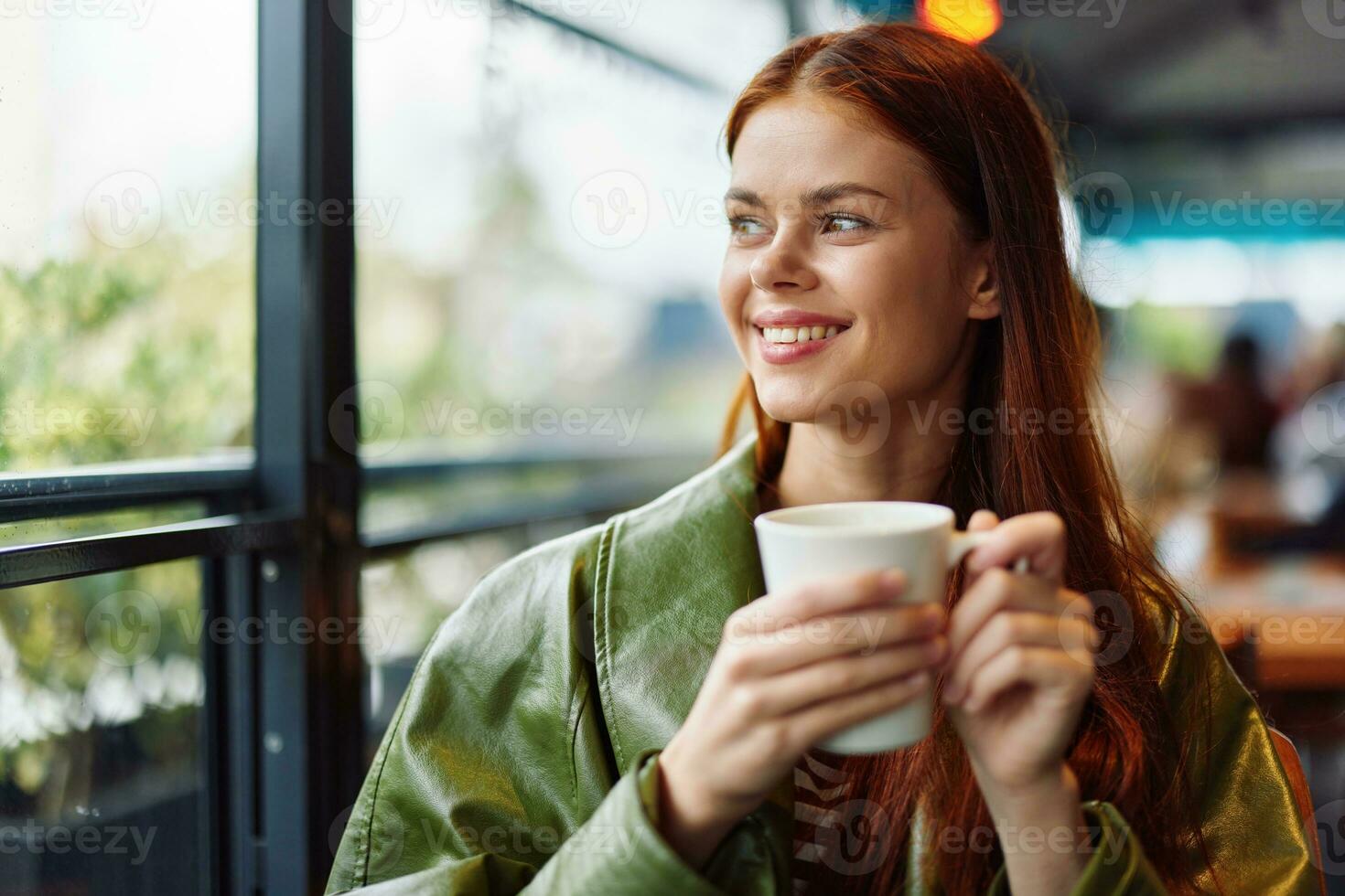 Portrait of a woman influencer drinking a drink from a mug in a cafe and smiling with her teeth looking out the window, content blogger close-up photo