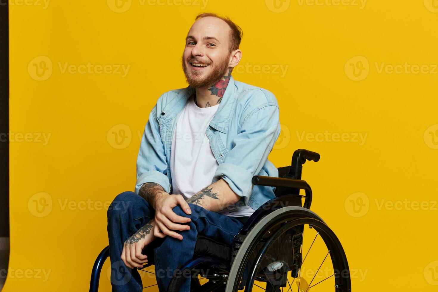 A man in a wheelchair smile and happiness, thumb up, with tattoos on his hands sits on a yellow studio background, the concept of health a person with disabilities photo
