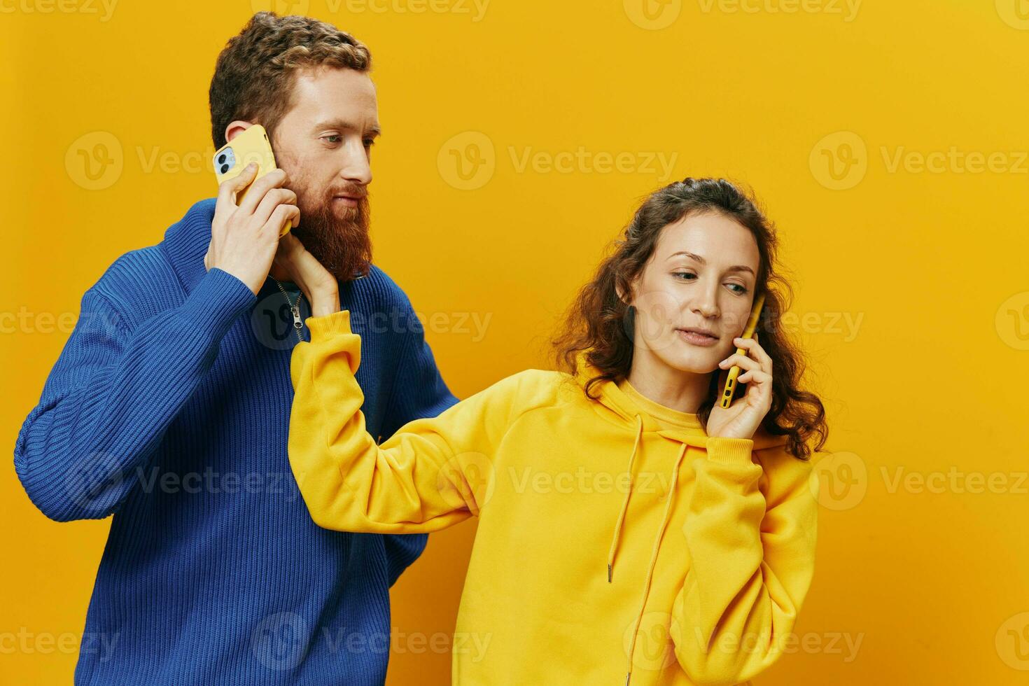 Woman and man cheerful couple with phones in hand talking on cell phone crooked smile cheerful, on yellow background. The concept of real family relationships, talking on the phone, work online. photo