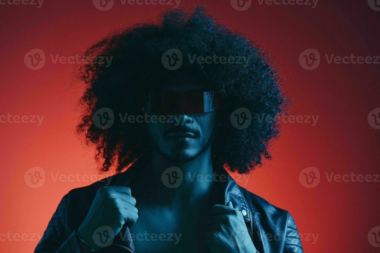 Portrait of fashion man with curly hair on red background with stylish glasses, multicultural, colored light, black leather jacket trend, modern concept. photo
