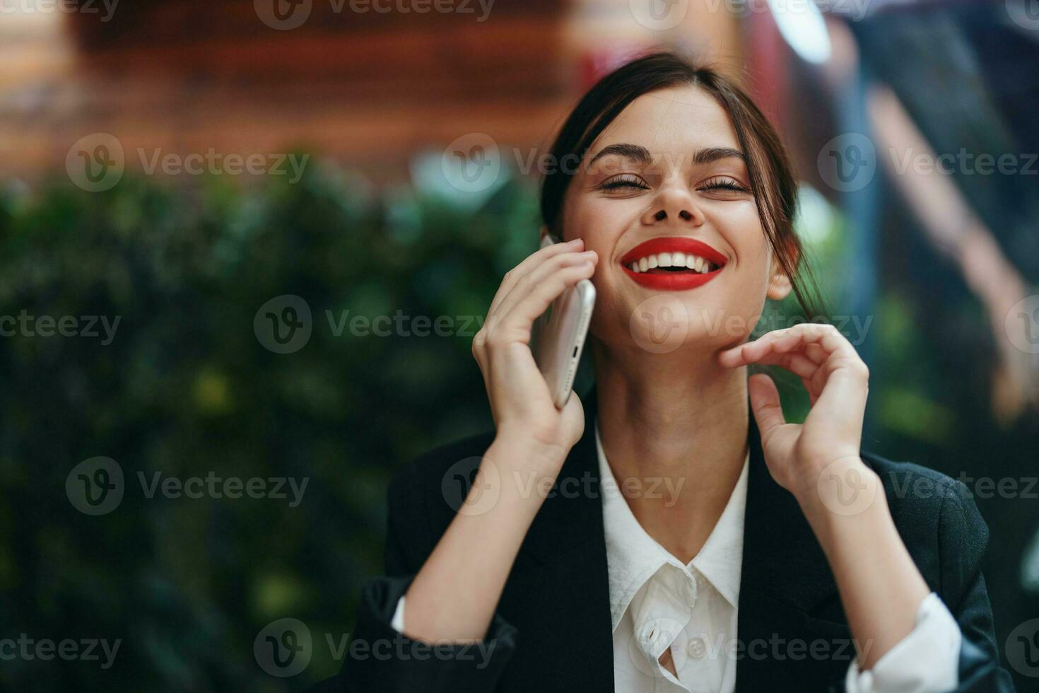 Woman blogger tourist sits in a cafe at a table with a phone in her hands conversation, mobile communication and internet in spring travel, video business call, freelance work online, smile with teeth photo