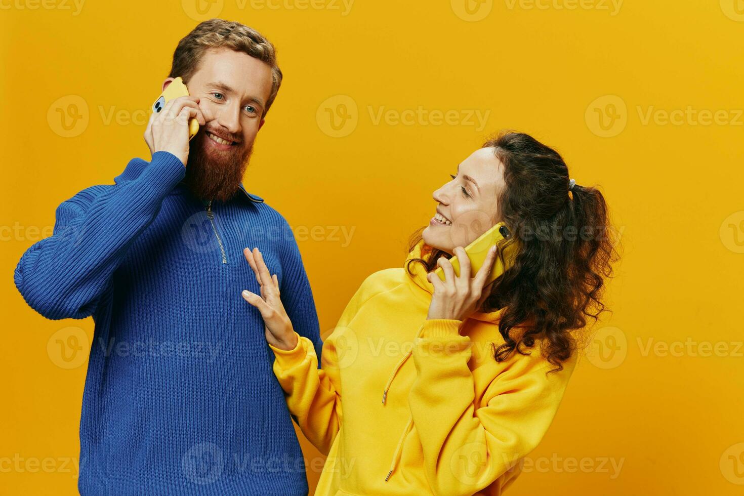 Woman and man cheerful couple with phones in hand talking on cell phone crooked smile cheerful, on yellow background. The concept of real family relationships, talking on the phone, work online. photo