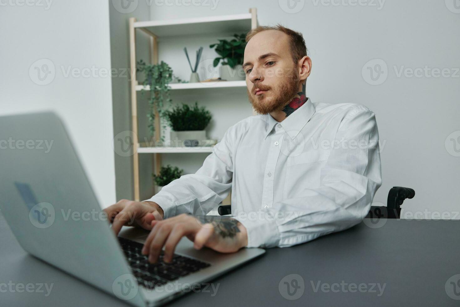 A man in a wheelchair a businessman with tattoos in the office works at a laptop, integration into society, the concept of working a person with disabilities, freedom from social frameworks photo