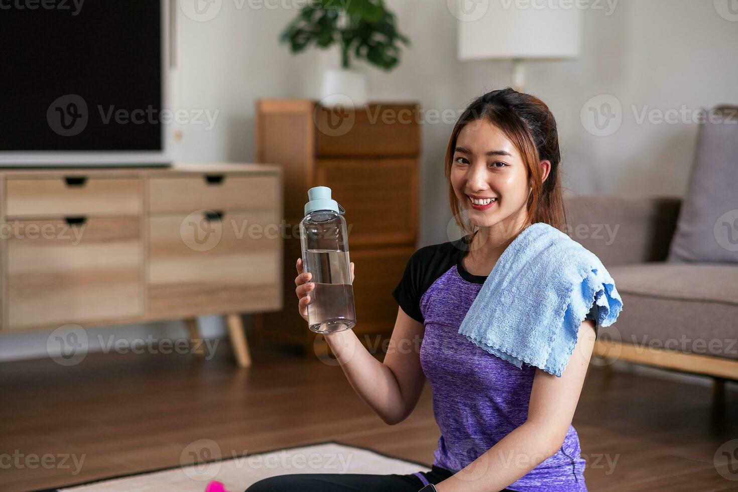 Asian woman taking break after exercise with drinking water at the home. home exercise concept. photo