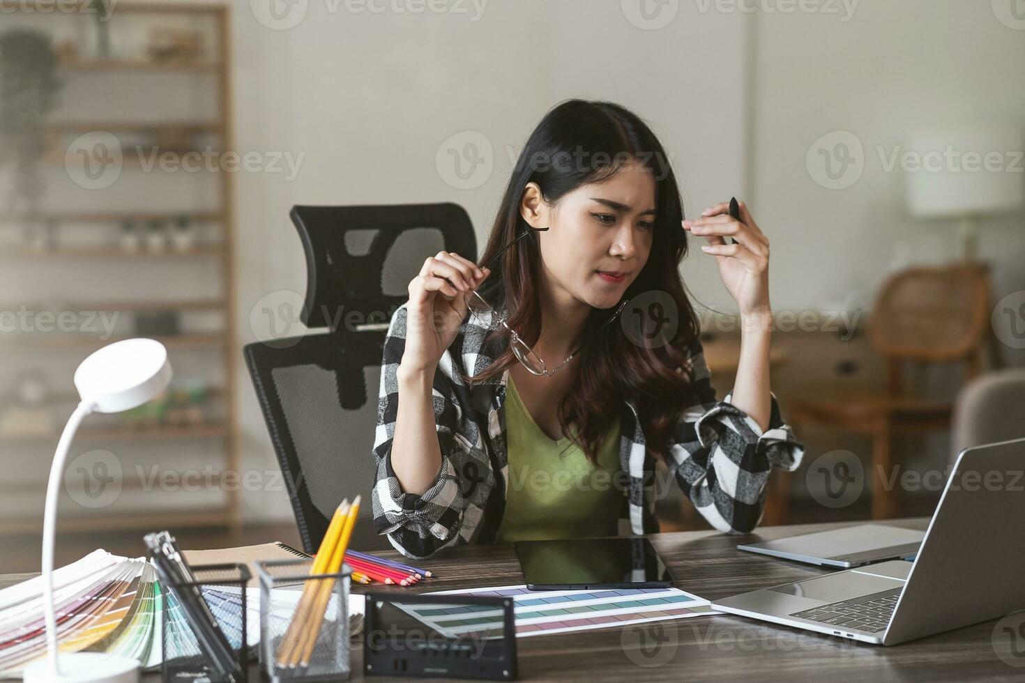 Serious and focused female graphic designer sitting at her desk, surrounded by sketches and drawings. photo