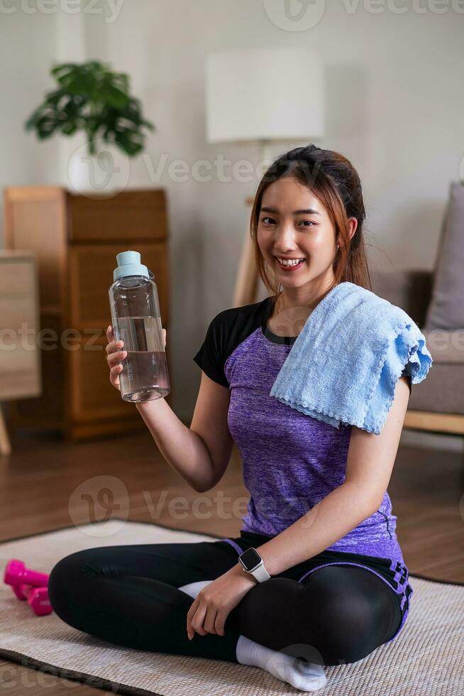 Asian woman taking break after exercise with drinking water at the home. home exercise concept. photo